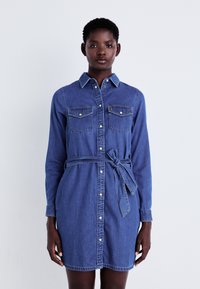 Denim skjortekjole, medium blå, knapp foran, to brystlommer, belte i midjen, lange ermer, klassisk krage, glatt tekstur.