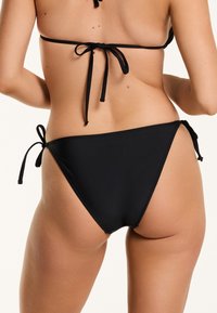 Fekete bikini alsó, oldalt megkötővel, sima textúrájú és minimalista dizájnnal, magasan szabott lábnyílásokkal.