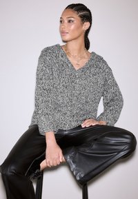 Teksturirani, sivi džemper s V-izrezom i savinutim manžetama, uparen s crnim kožnim hlačama. Zlatni slojeviti lančići dodaju detalj.