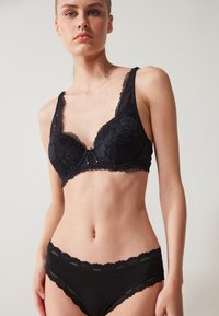 Μαύρο δαντελένιο μπραλέτα με κοφτές άκρες; διαθέτει floral σχέδιο και διακοσμητικό φιόγκο στη μέση. Μαύρα δαντελένια παντελόνια με τόξο.