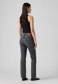 Zwarte tanktop gecombineerd met hoge, rechte grijze jeans met achterzakken en een leren label op de tailleband.