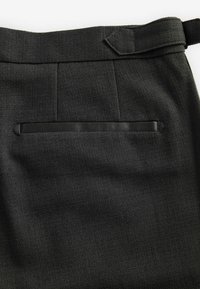 Pantalones negros texturizados con una cinturilla suave, que cuentan con un bolsillo trasero plano con un ribete de satén negro. Diseño a medida sin cierres visibles.