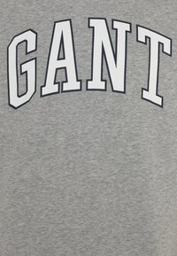 Felpa grigia con grandi lettere bianche a blocchi che spelling "GANT" sul petto. Il testo ha un contorno scuro per un migliore contrasto. Texture morbida.