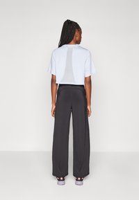 Lichtblauw cropped t-shirt met een gaaspaneel op de rug, gecombineerd met zwarte brede broek en sportieve schoenen met roze accenten.