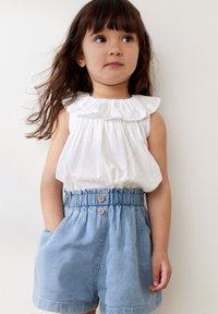 Blusa bianca senza maniche con scollatura a volant e tessuto texturizzato; pantaloncini in denim con vita elastica, due bottoni e tasche laterali.