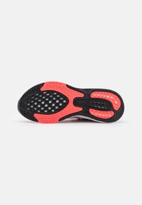 Semelle extérieure de chaussure de sport avec une base en caoutchouc noir, des accents rouges, des motifs de grip texturés et une structure en nid d'abeille pour la traction.
