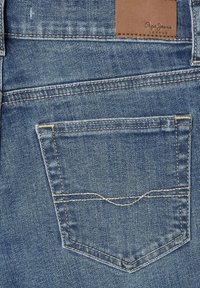 Tamno plave traperice s stražnjim džepom, vidljivim šavovima u svijetlo žutoj boji i smešnom kožnom etiketom sa natpisom "Pepe Jeans London."