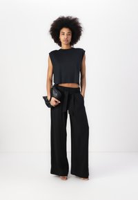 Top corto negro sin mangas combinado con pantalones negros de pierna ancha con una cintura anudada y un pequeño bolso negro.