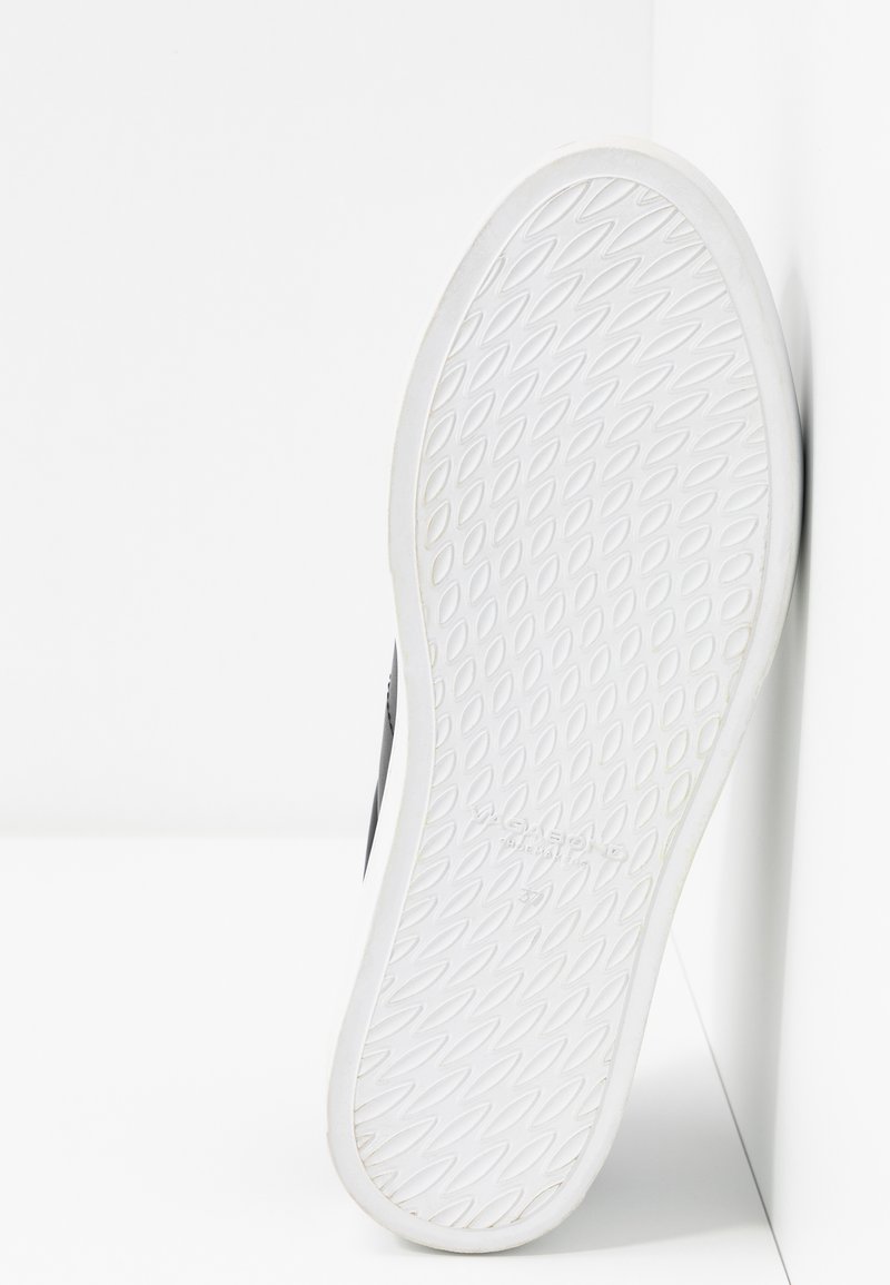 Schwarze Sneaker-Sohle mit einem strukturierten weißen Gummiboden, der ein Rautenmuster zeigt und eine glatte Oberfläche sowie abgerundete Kanten aufweist.