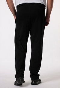 Schwarze Jogginghosen mit elastischem Bund, geraden Beinen und seitlichen Taschen. Getragen mit schwarzen Sportschuhen. Glatte Stoffstruktur.