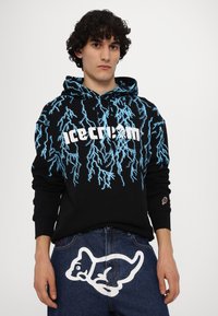 Black hoodie with blue lightning print and "icecream" logo. Paired with blue denim jeans featuring a large white cartoon dog graphic.