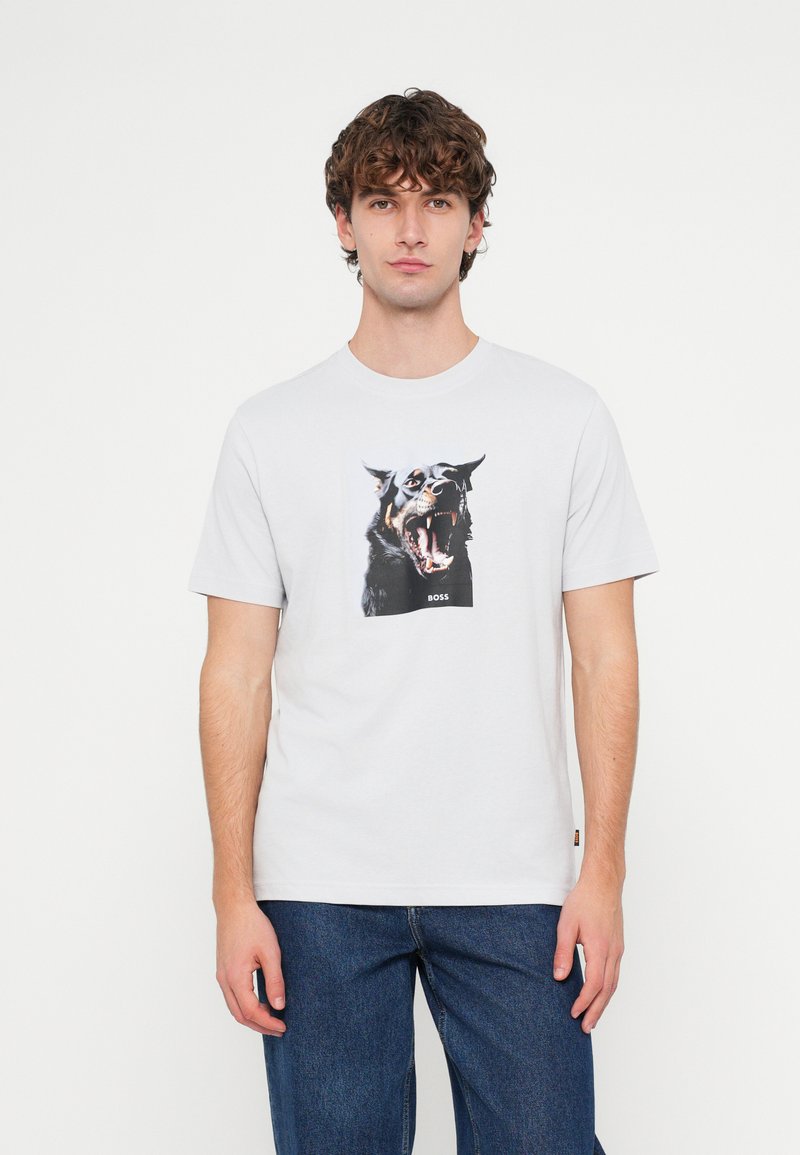 Λευκό βαμβακερό t-shirt με γραφικό ενός μαύρου σκύλου που γαβγίζει και την επιγραφή «BOSS». Εφαρμοστή σχεδίαση με κοντά μανίκια και στρογγυλή λαιμόκοψη.
