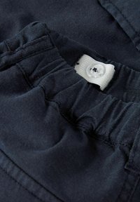 Navy blue pants with an elastic waistband, featuring a white button closure and textured fabric. Close-up view of the waist area.