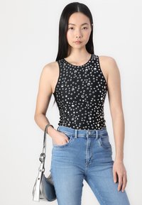 Top sin mangas negro adornado con tachuelas plateadas y un escote redondo, combinado con unos jeans de tiro alto azul claro y un bolso de hombro plateado.