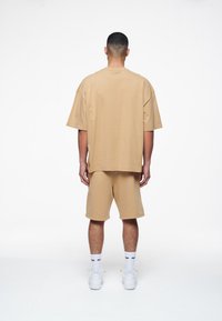 Tan oversized t-shirt og matchende shorts lavet af blødt stof. Bagudperspektiv som viser korte ærmer, afslappet pasform, og shorts der går til midten af låret.