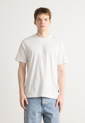White cotton short-sleeve T-shirt with a round neckline and straight hem. Paired with light blue denim jeans. Simple and minimal design.