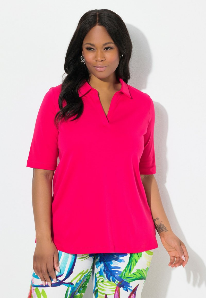 Fuchsia poloshirt met een kraag en korte mouwen, gemaakt van gladde stof; gecombineerd met gekleurde broeken met bladprint.