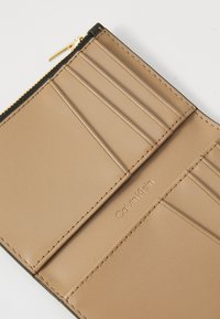 Beige skinn bifold lommebok med flere kortlommer, en glidelåslomme til mynter med gullglider, og preget Calvin Klein-logo.
