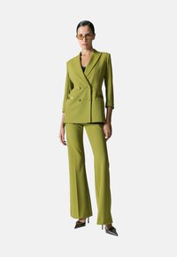 Blazer doppiopetto e pantaloni abbinati in un vivace verde oliva, caratterizzati da un design sartoriale, una texture liscia e una vestibilità ampia.