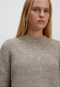 Lichtbeige gebreide trui met een geribbelde structuur, ronde halslijn en lange mouwen. Zacht materiaal met subtiele kleurvariaties.