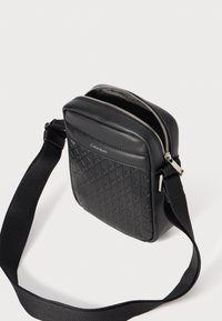 Sac bandoulière noir en cuir texturé, doté d'un motif en losange, d'une fermeture éclair argentée et d'une bandoulière en tissu réglable. Logo affiché à l'avant.