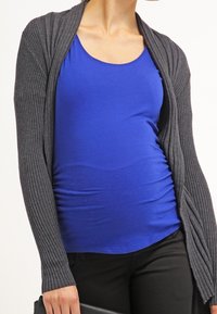 Cárdigan de canalé gris oscuro sobre una camiseta de tirantes azul royal, complementado con pantalones negros. El conjunto es casual y ajustado.