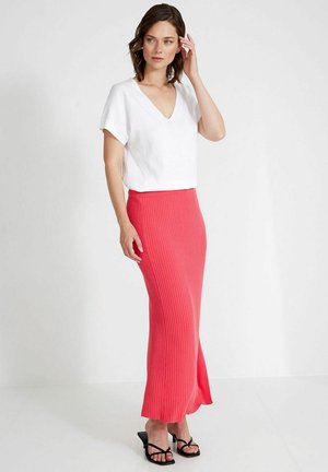 Weißes kurzärmeliges V-Neck-Top kombiniert mit einem gerippten, knöchellangen korallfarbenen Rock. Das Modell trägt schwarze Riemchensandalen. Einfaches, klares Design.