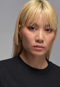 Mustmust kaelusega must särk, mille kannab inimene sirgete, heledate blondide juustega ning diskreetsete kuldsete kõrvarõngastega. Loomulik nahatekstuur nähtav.