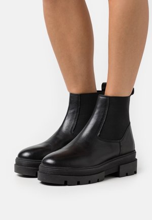 Bottines en cuir noir avec panneaux latéraux élastiques, semelle en caoutchouc épaisse et finition lisse. Comprend une languette pour un enfilage facile.