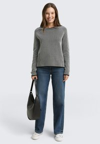 Szary sweter w paski z długimi rękawami, zestawiony z niebieskimi spodniami typu wide-leg i białymi trampkami. Czarna torebka na ramię jako akcent.