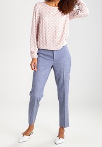Maglietta a maniche lunghe rosa chiaro con un motivo floreale, abbinata a pantaloni blu a quadri alla caviglia e scarpe bianche con punta.