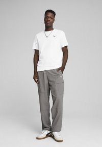 Hvid T-shirt med rund hals og lille sort logo, grå cargo-bukser med lommer og hvide sneakers med brune detaljer; casual streetwear stil.