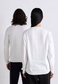 White knit sweaters with ribbed hems and cuffs, viewed from the back. One sweater features a classic crew neckline, the other slightly different.