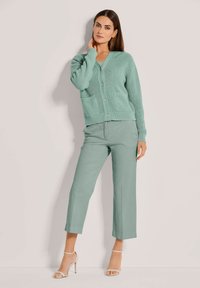 Hellgrüner strukturierter Cardigan mit V-Ausschnitt und Knopfverschluss, kombiniert mit passenden, taillierten Hosen und nackten Riemchen-Heels.