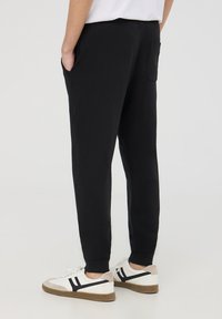 Pantaloni della tuta neri con una vestibilità rilassata, tasche laterali e una vita a coste, abbinati a sneaker bianche con dettagli neri e una suola strutturata.