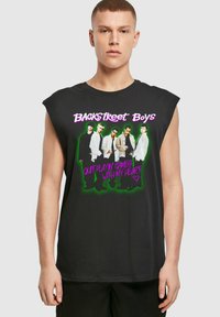Musthave musta ilma varrukatega T-särk, millel on grafika tekstiga "Backstreet Boys" ja pildi viiest mehefiguurist ees.