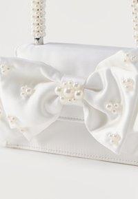 Λευκό τσαντάκι από σατέν με μεγάλο φιόγκο από σατέν, στολισμένο με μικρές πέρλες και λαβές διακοσμημένες με χάντρες πέρλας που ταιριάζουν.