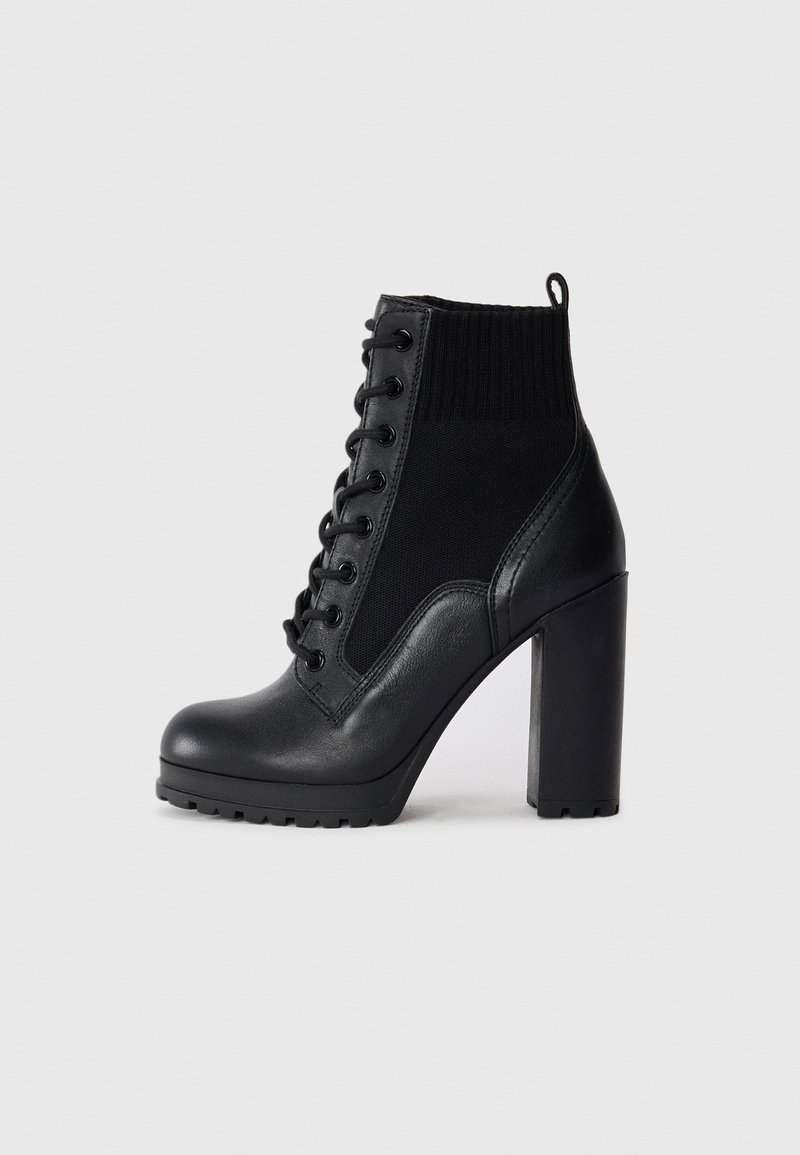Bottine noire en cuir et maille avec lacets à l'avant, talon haut épais et languette à l'arrière.