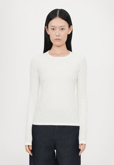 Haut blanc à manches longues avec un motif en grille texturé. Présente un col rond et une coupe ajustée, associé à un pantalon large noir.