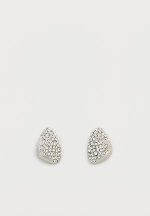 Petites boucles d'oreilles triangulaires en argent ornées de strass clairs regroupés sur un fond blanc.