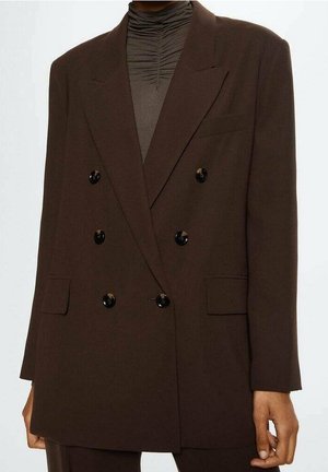 Blazer marron foncé croisé à six boutons noirs porté sur un col roulé froncé foncé, associé à un pantalon marron assorti.