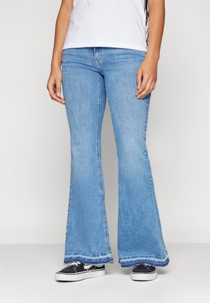 Light blue flared jeans made of denim with a faded finish, featuring frayed hem details and paired with black sneakers.