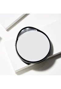 Miroir rond avec une surface réfléchissante lisse, encadré dans un cadre en plastique noir. Dispose d'une poignée intégrée pour la portabilité.