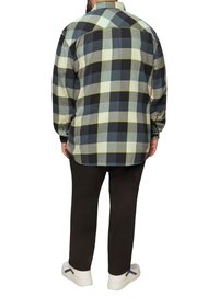 Flanellen overhemd met een groen, marineblauwe en zwarte ruitpatroon, lange mouwen, knoopmanchetten en een afgeronde zoom, gecombineerd met zwarte broek en witte sneakers.