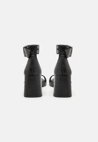 Sandali con tacco in pelle nera con cinturino alla caviglia, dotati di hardware in metallo e di un tacco a blocco, che mettono in mostra una texture liscia e opaca.