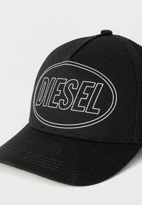 Μαύρο μπερέ με καπάκι από ύφασμα με δομημένο σχήμα. Διαθέτει ανάγλυφο, λευκό λογότυπο "DIESEL" μέσα σε οβάλ περίγραμμα.