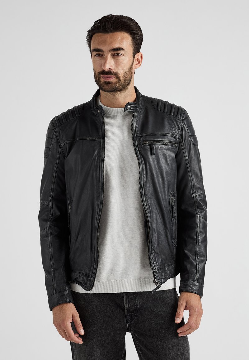 Sort læderjakke med rillede skulderdetaljer, lynlåslommer og høj krave. Bæres over en grå sweater og mørke jeans.