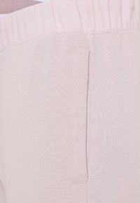 Ljusrosa byxor i mjukt, texturerat tyg med elastiskt midjeband och sidofickdetalj. Tyget ser slätt och lättviktigt ut.