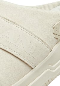 Beige semsket slip-on sko med en teksturert overflate, med en bred stropp merket "KANI" og en solid gummisåle.