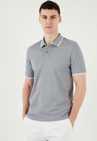 Pilkas polo marškinėliai su švelnia tekstūra, trumpomis rankovėmis ir dviem mygtukais. Baltos detailės ant apykaklės ir rankovių kraštų.